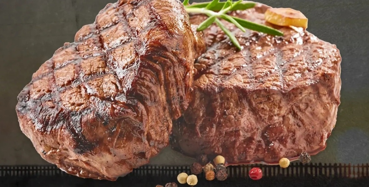 Two thick grilled steaks with char marks, rosemary and peppercorns