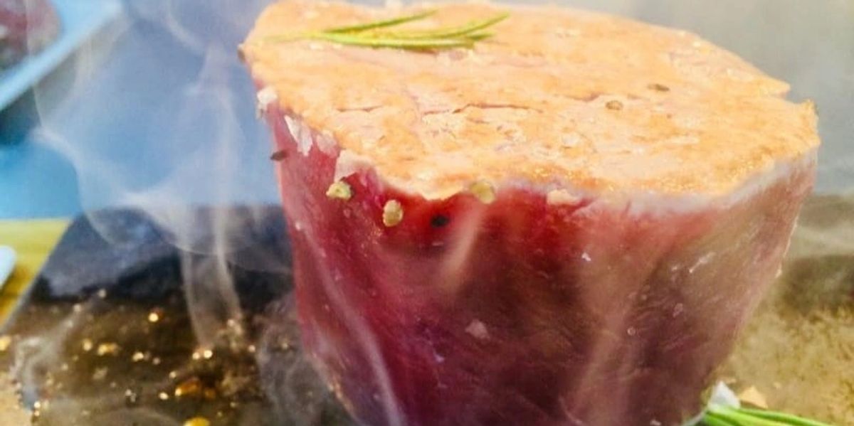A thick cut of meat with rosemary and coarse salt sizzling on the hot stone, smoke rising
